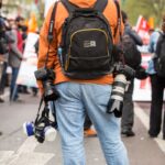 journaliste professionnel en jean bleu et sac à dos orange marchant dans la rue pendant la journée
