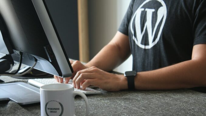 Entraide entre webmasters et rédacteurs du web : Un levier essentiel pour la réussite digitale Webmaster Wordpress en t-shirt noir et blanc utilisant un ordinateur